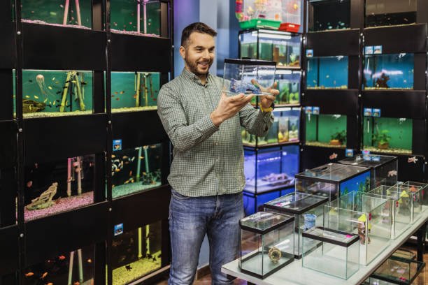 Handsome middle age man choosing and buying exotic fishes in modern pet shop.